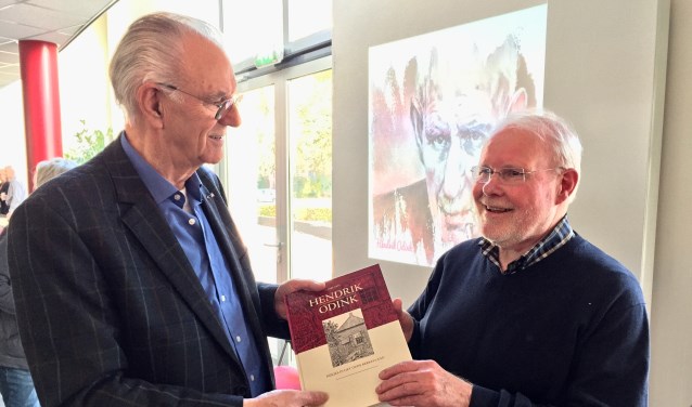 Ben Tragter (r) reikt het eerste exemplaar met niet eerder uitgebracht werk van Hendrik Odink uit aan achterneef Gerrit Odink (l) in Kulturhus 't Spieker in Eibergen. Foto: Susanne ten Have