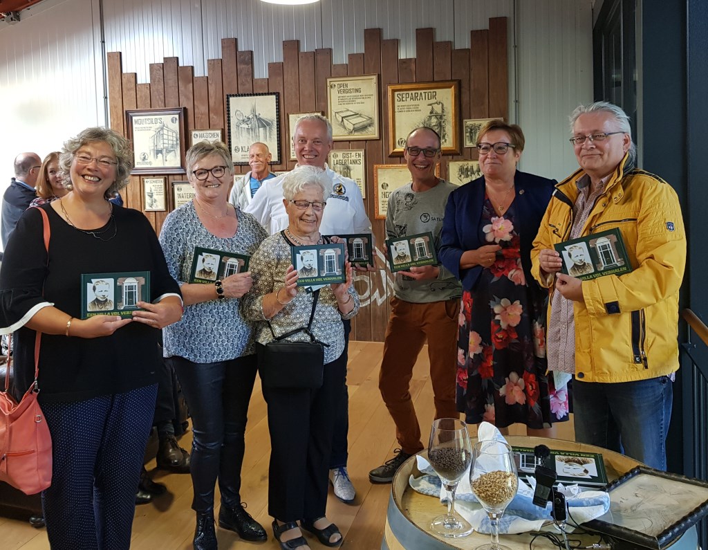 Irmgard Bomers heeft zojuist haar moeder (midden voor) het eerste exemplaar overhandigd, staand tussen hen die op hun manier een band met het pand hebben. Foto: Henri Walterbos