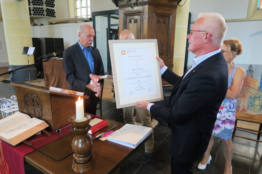 Dominee Wim Blanken bekijkt de oorkonde, behorende bij het door hem ontvangen Draaginsigne in Goud met Briljant. Foto: Theo Huijskes