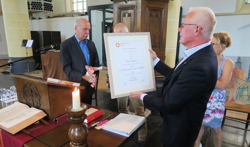 Dominee Wim Blanken bekijkt de oorkonde, behorende bij het door hem ontvangen Draaginsigne in Goud met Briljant. Foto: Theo Huijskes