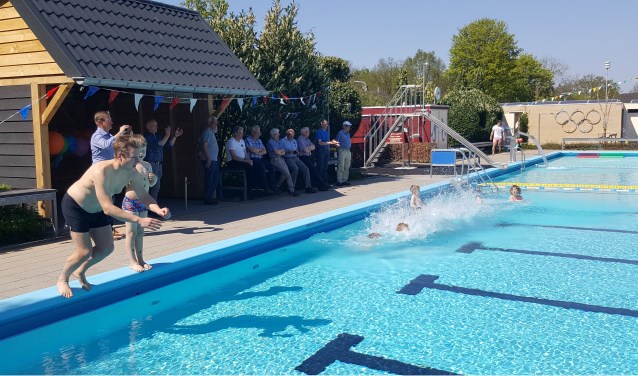 Rogier Vroeg in de Wei en zoon Rubèn duiken het pas geopende zwembad in, toegekeken door publiek in De Hut dat vrijdagmiddag eveneens werd geopend. Foto: Marjan Lijftogt
