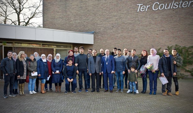 Loco-burgemeester Fred Dellemijn, Aziz Azizi en Tineke Parson temidden van de zeventien statushouders, hun families diverse vrijwilligers van vluchtelingenwerk