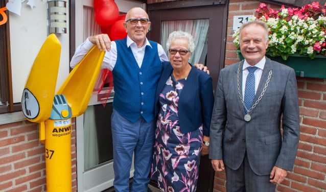 Jan en Renée met de burgemeester voor de deur van hun huis, waar de Wegenwachtpaal herinnert aan het werk van Jan bij de ANWB.