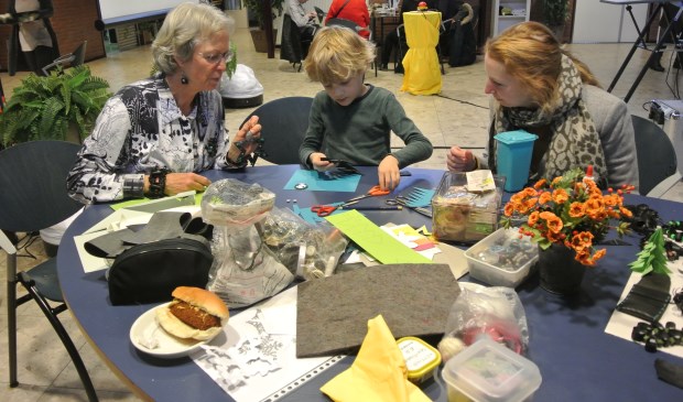 Siem maakt aan de knutseltafel, onder toeziend oog van vrijwilliger Truus, figuurtjes uit gerecycled materiaal.