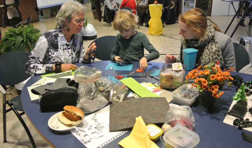 Siem maakt aan de knutseltafel, onder toeziend oog van vrijwilliger Truus, figuurtjes uit gerecycled materiaal.