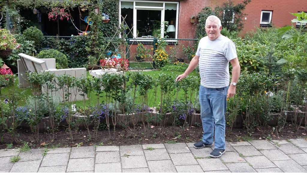 Pieter Pols voor zijn fraaie tuin met bloemen, gras en bank.