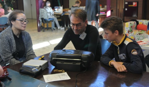 Reparateur Koert (midden) kijkt een radio-cd speler na met hulp van stagair Pieter (rechts). Op de achtergrond verstellen naaisters Magda en Tiny kleding. (foto Frans Poot)