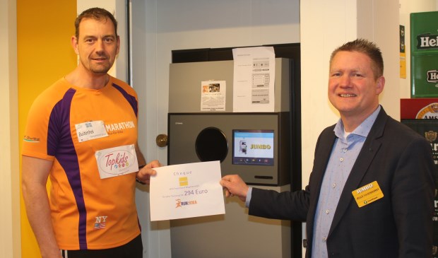 Nico Sturkop en Jelle Farenhorst bij het nieuwe apparaat van Jumbo met de cheque van bijna 300 euro, die de klanten al aan KIKA doneerden.