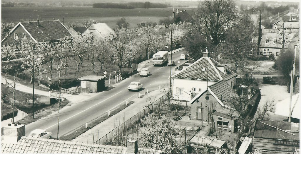 Deze foto van het kruispunt bij het voormalig gemeentehuis van Maartensdijk is in de jaren zestig van de vorige eeuw door wijlen Jaap Eits vanaf de brandweertoren gemaakt. De fruitbomen bij de hoeve Persijn van boer De Rooij staan al in bloei, terwijl de kastanjeboom voor het gemeentehuis nog aan de lente moet beginnen. De foto is voor 1968 gemaakt, want de Tolakkerweg is nog niet verbreed. Wim de Rooij vertelde, dat in augustus 1968 van zij