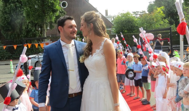Het bruidspaar wordt door alle groepen van de school enthousiast verwelkomd en toegejuicht.