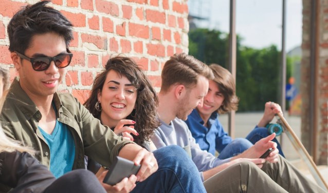Group of young multiethnic friends sitting on the floor chatting to each other having fun using smartphone - social network,technology, communication, technology concept