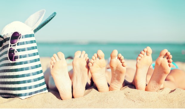 summer vacation, sunbathing and pedicure concept - three women lying on the beach with straw hat, sunglasses and bag