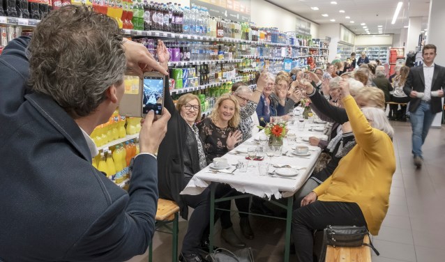 • Supermarkteigenaar Erik Wiersma van de Albert Heijn in Krimpen aan de Lek neemt een foto van de gasten die hun eten kregen geserveerd aan een lange eettafel.