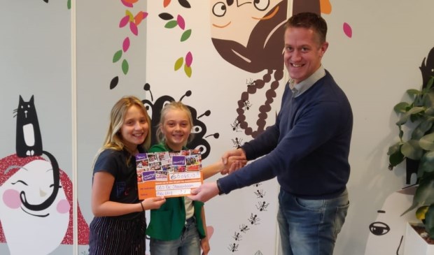 • Interim-directeur Rogier Levy overhandigt de cheque aan de initiatiefneemsters van de sponsorloop, Roos en Sophie.