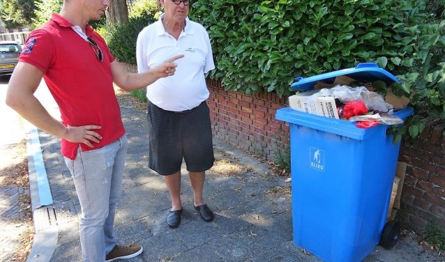 Raadslid Gijs Dupont en een omwonende inspecteren de overvolle blauwe containers die er al lange tijd staat (foto: Ap de Heus).