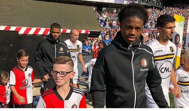 Jaydey van der Kleij (8) uit Leidschendaman loopt aan de hand van verdediger Tyrell Malacia het veld op in de kuip.