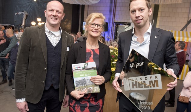 Gijs van der Helm (met een cadeau van de medewerkers) en Anton Dijkshoorn overhandigden het eerste exemplaar van het jubileummagazine aan Marja van der Helm. (Foto: Cok van den Berg)