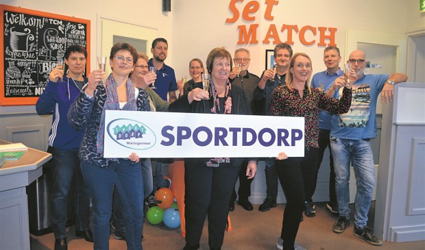 Wethouder Mary van Gent toont een Sportdorp-bord temidden van de partners van Sportdorp Wieringermeer.