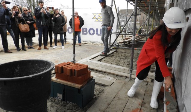 Bewoners maken foto's van de eerste steenlegging door de wethouder.