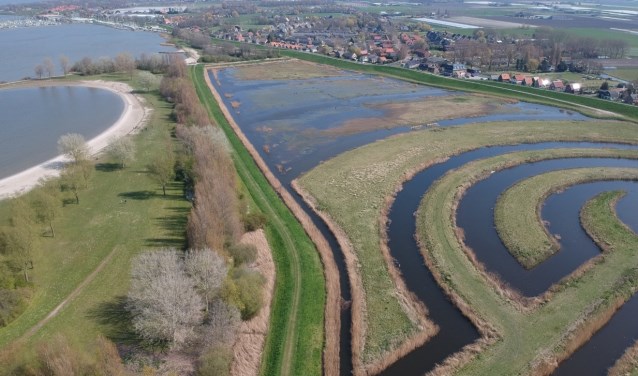 Deelnemers verzamelen bij de parkeerplaats achter de dijk (bovenaan de foto).