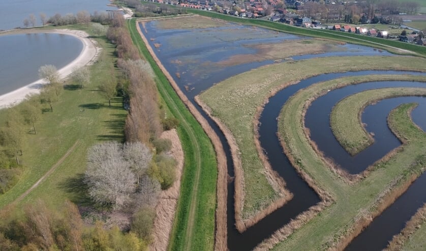 Deelnemers verzamelen bij de parkeerplaats achter de dijk (bovenaan de foto).