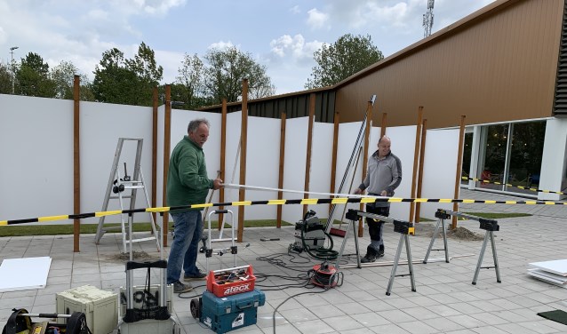 De bouwers van de nieuwe buitenkleedhokjes monteren de eerste deur. Met het mooie weer op komst kan iedereen zich hier voortaan fatsoenlijk omkleden.
