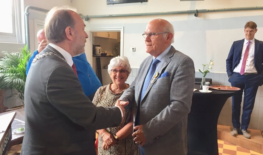 Burgemeester Bert Blase (l) feliciteert Nico Klaver met zijn kersverse Koninklijke onderscheiding; mevrouw Klaver kijkt trots toe.