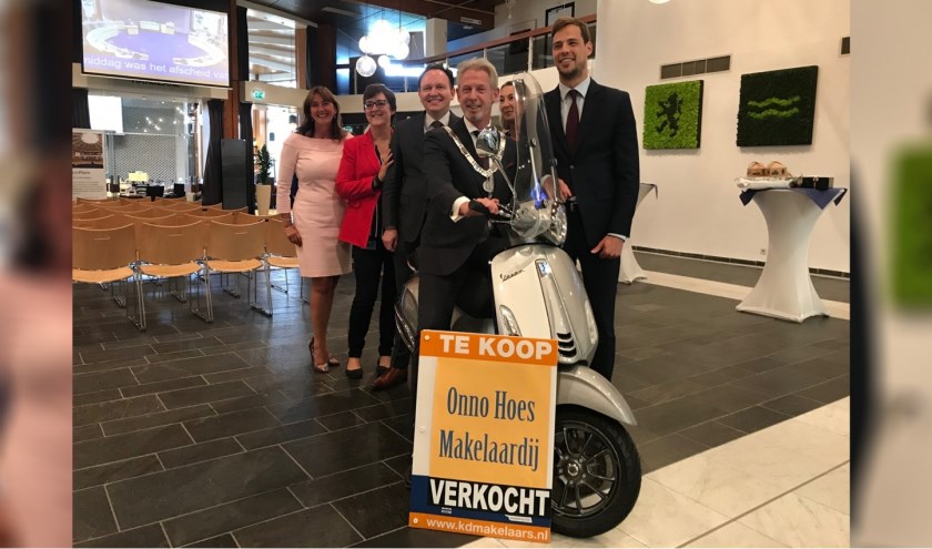 Waarnemend burgemeester Onno Hoes poseert in de raadszaal op de zojuist overhandigde makelaarsscooter.