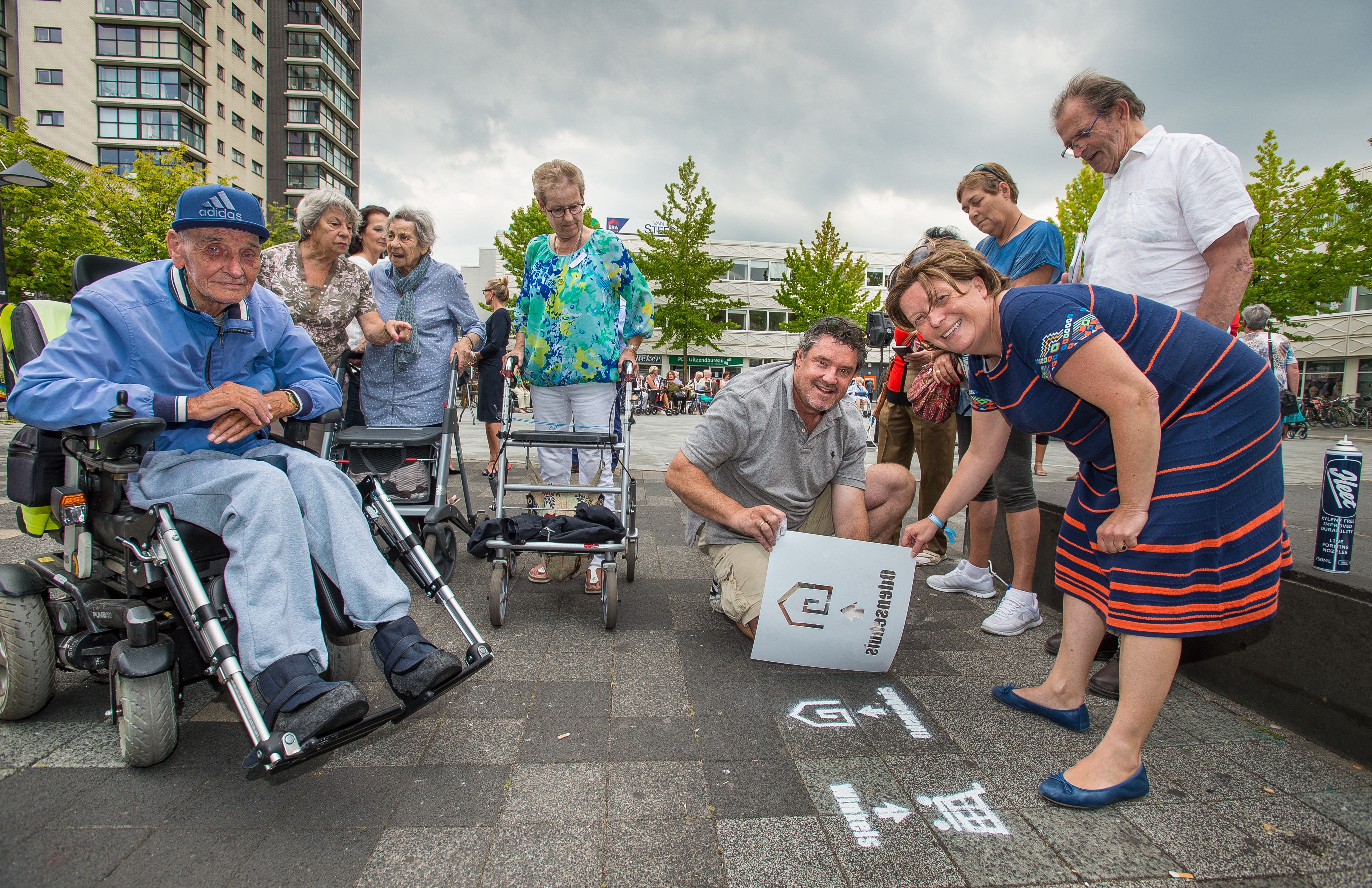 Stadsdeelbestuurder Esther Lagendijk heeft zojuist de laatste symbolen aangebracht waarmee zij de boodschappenroute officieel heeft geopend. Links naast haar Jim Bowes van Natural Media Experts. Om hen heen bezoekers van het Odensehuis en buurtbewoners. (Foto: Richard Mouw)