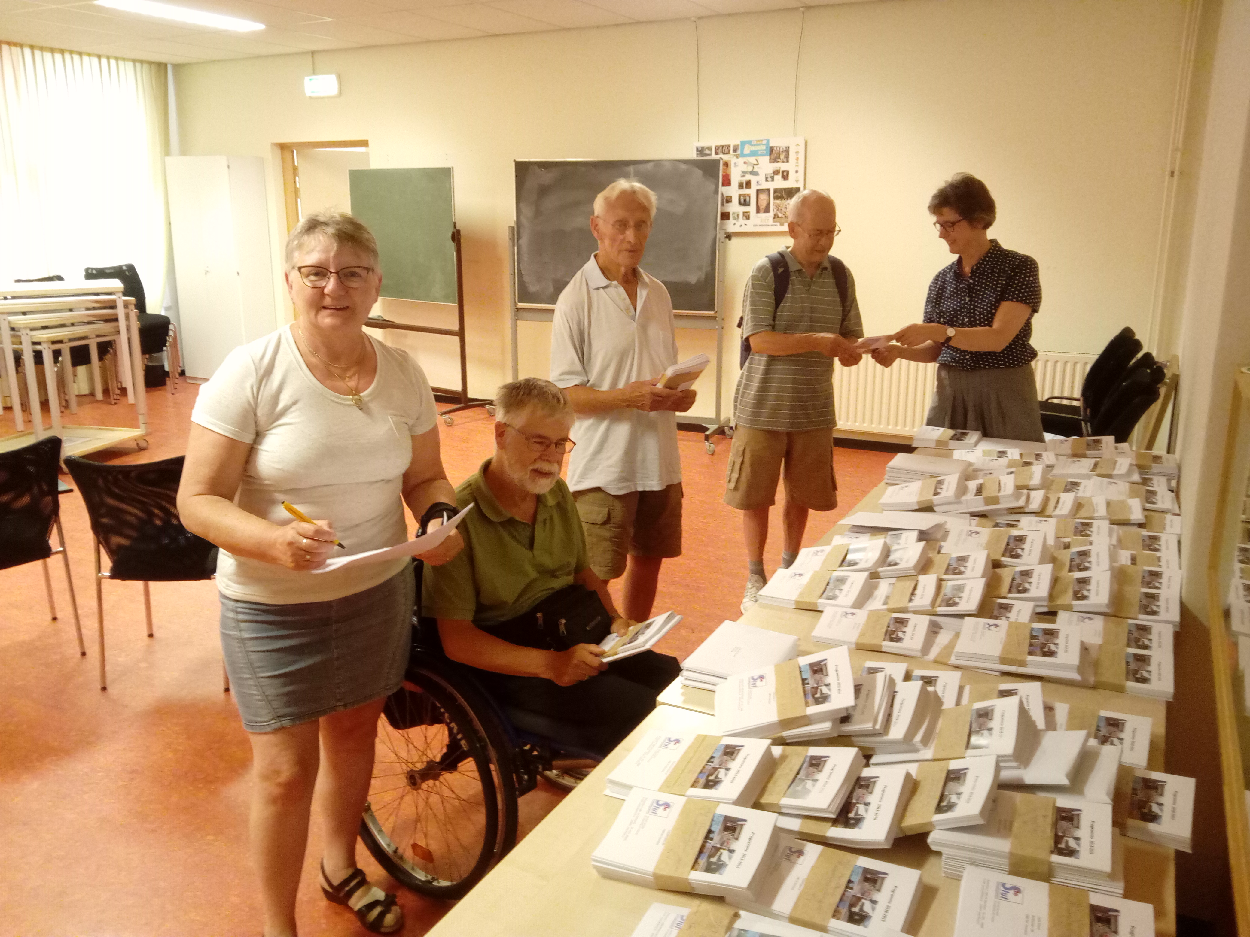 Coördinator Erna van Kempen (uiterst rechts) deelt de programmaboekjes uit aan vrijwilligers die de boekjes bezorgen. (Foto: Bos Media Services)