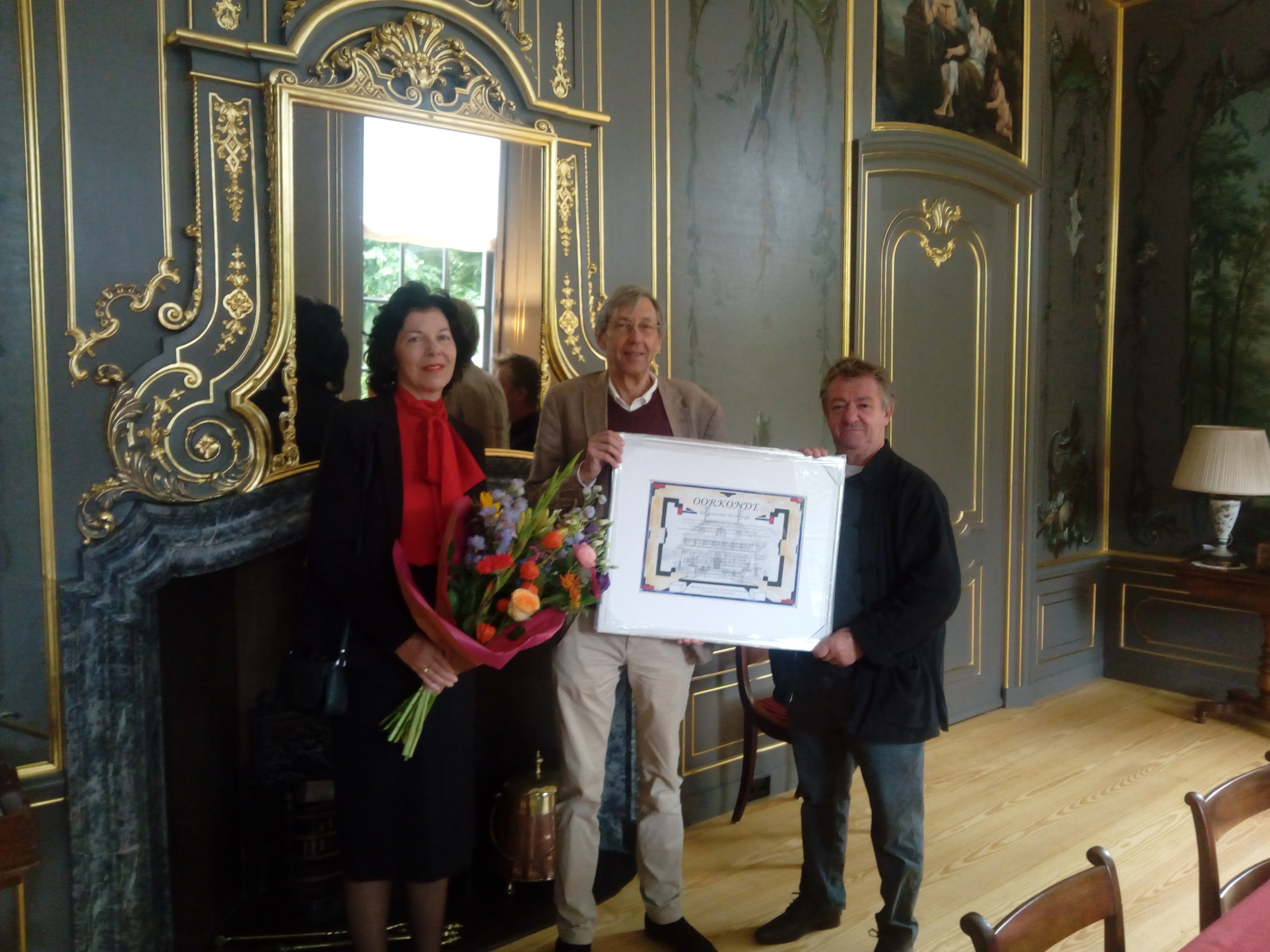 In de volledig gerestaureerde tuinkamer van Akerendam werd de oorkonde door wethouder Hanneke Niele aan mr. Koeno Sluyterman van Loo overhandigd. Rechts van hen beeldend kunstenaar Louis 't Hart, hij vervaardigde de oorkonde in opdracht van de gemeente Beverwijk. (Foto: Bos Media Services)