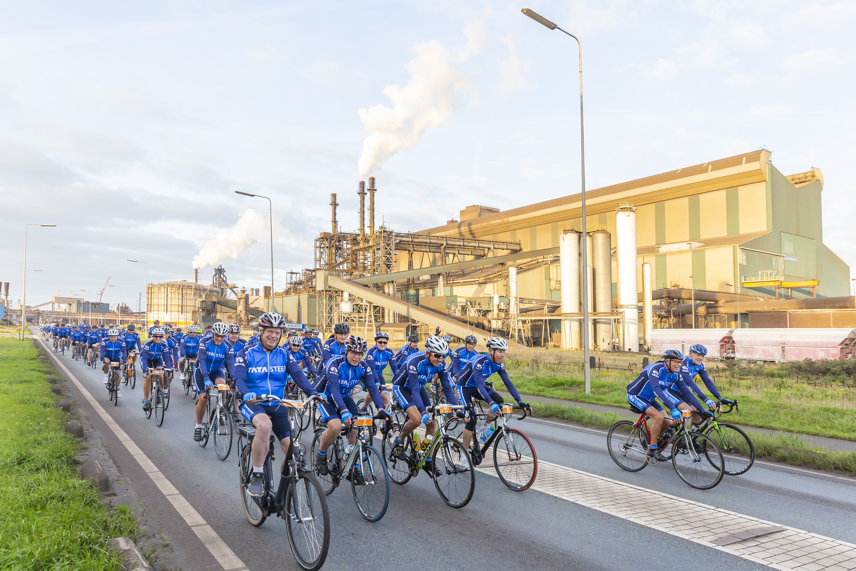 De wielrenners bij het passeren van de staalfabriek, met linksvoor Hans Fischer, CEO van Tata Steel in Europa. (Foto: Tata Steel)