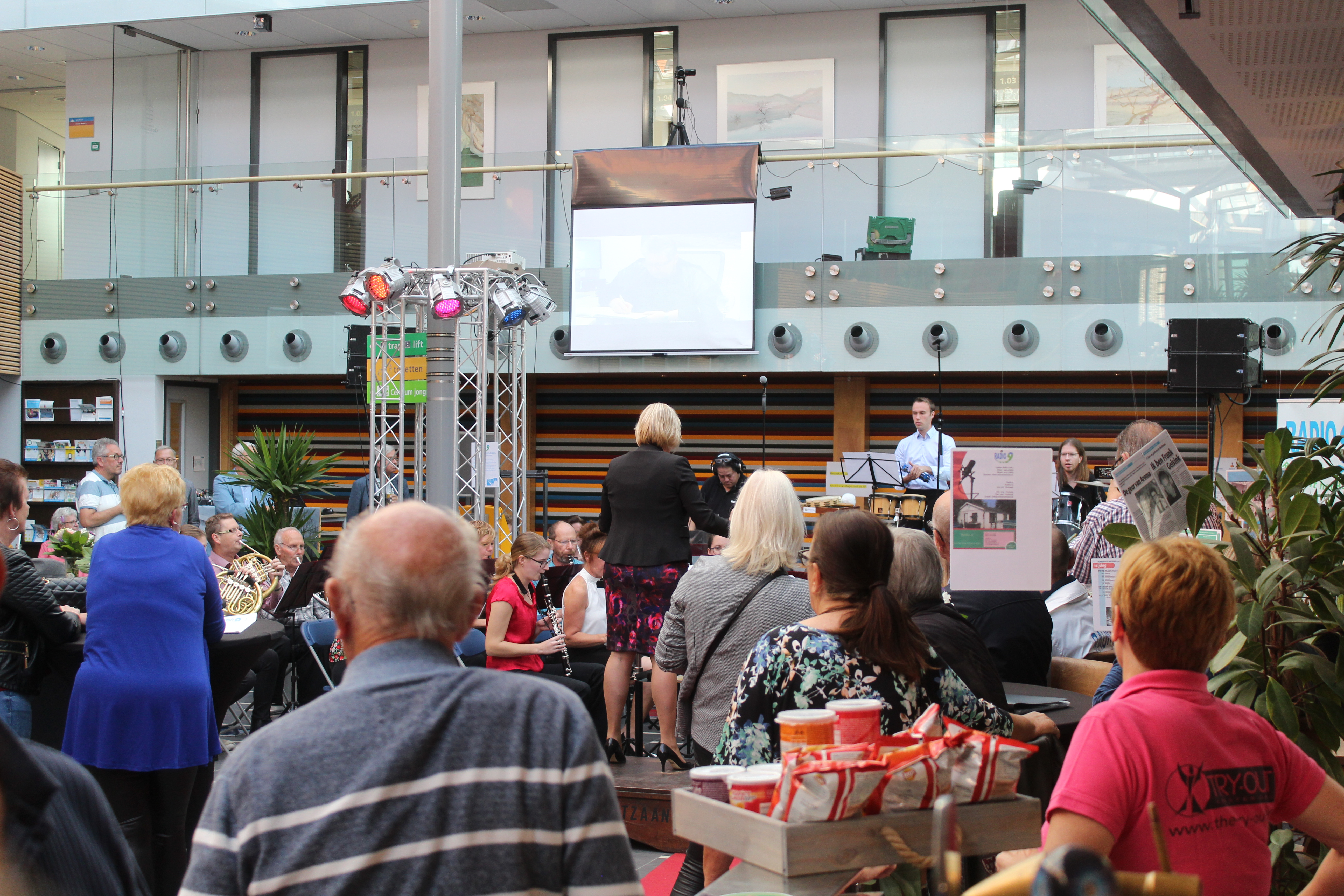 Receptie Radio 9 in het Atrium. Burgemeester Meerhof feliciteert Programmaleider Nils Römer. Feestelijke bijdrage van het Popkoor. (Foto's: JWvD)