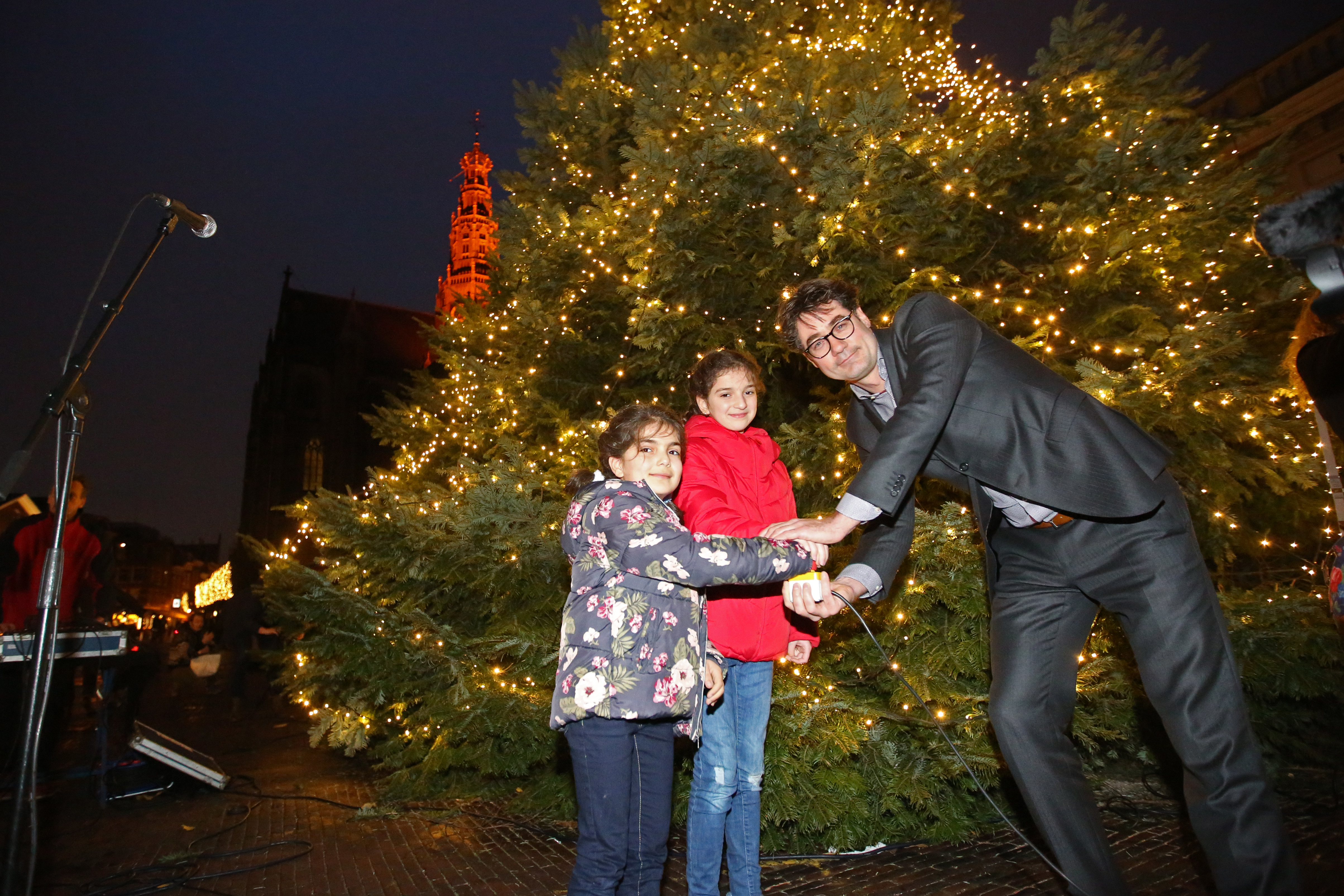 Wethouder Merijn Snoek poseert met de zusjes voor de gigantische kerstboom op de Grote Markt. (Foto: Rowin van Diest)