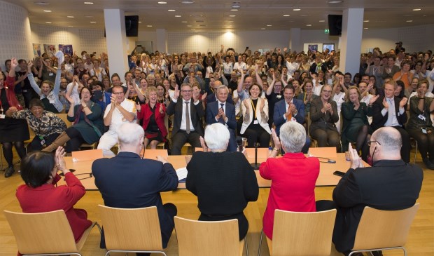 Een volle zaal met medewerkers reageert uitgelaten op het moment dat de positieve uitslag bekend wordt gemaakt.