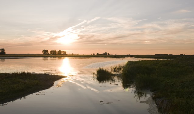 De zon zien wegzakken boven het weerspiegelende water. Ervaar de schoonheid van de natuur.