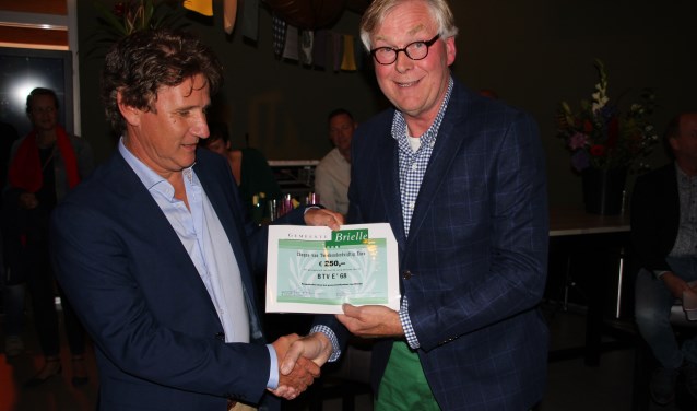 Voorzitter Frank Abrahams wordt gefeliciteerd door wethouder André Schoon en ontvangt een jubileumcheque van de gemeente Brielle