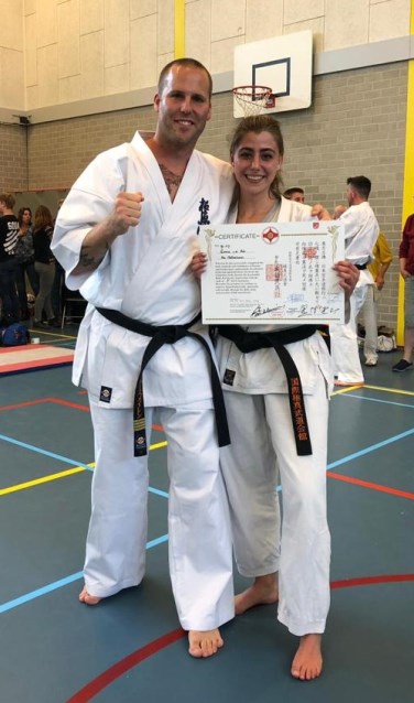 Emma van de Hul (rechts) samen met haar instructeur Jacques van Roosmalen en het bij de zwarte band bijbehorende diploma.
