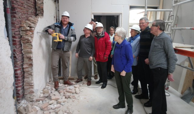 Wethouder Thomas Melisse sloopt de muur onder toeziend oog van bestuur en vrijwilligers. FOTO MONICA VERSLUIS
