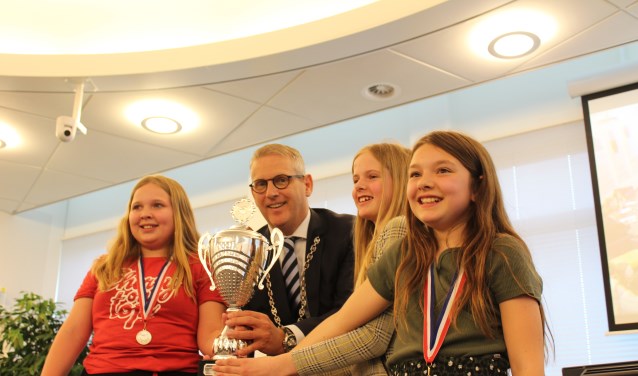 Burgemeester Van den Belt houdt, samen met leerlingen van de Gummarusschool, trots de winnaarsbeker vast met rechts voor beste debater Joannie Welleman.