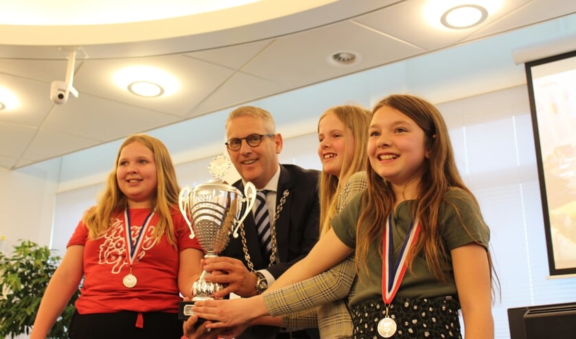 Burgemeester Van den Belt houdt, samen met leerlingen van de Gummarusschool, trots de winnaarsbeker vast met rechts voor beste debater Joannie Welleman.