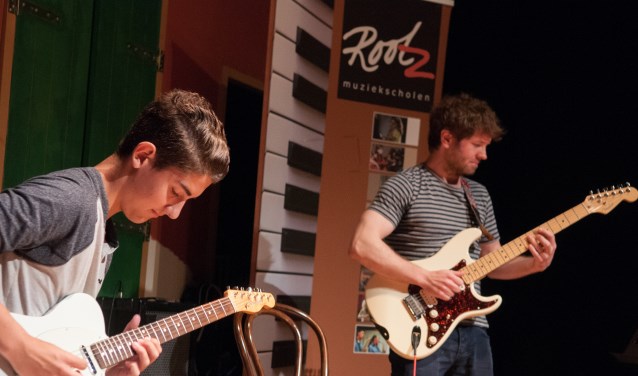 Twee leerlingen van de muziekschool bespelen hun guitaar.
