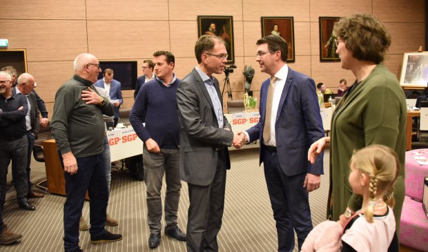 Wethouder Peter Hoek (SGP) schudt Peter Kraamer de hand. Rechts van Kraamer zijn vrouw Annemarie en één van zijn dochters.