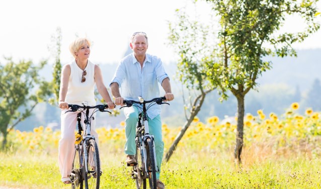 Senior couple, woman and man, riding their bikes along field of sunflowers