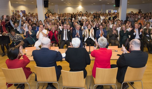 een volle zaal met medewerkers reageert uitgelaten op het moment dat de positieve uitslag bekend wordt gemaakt