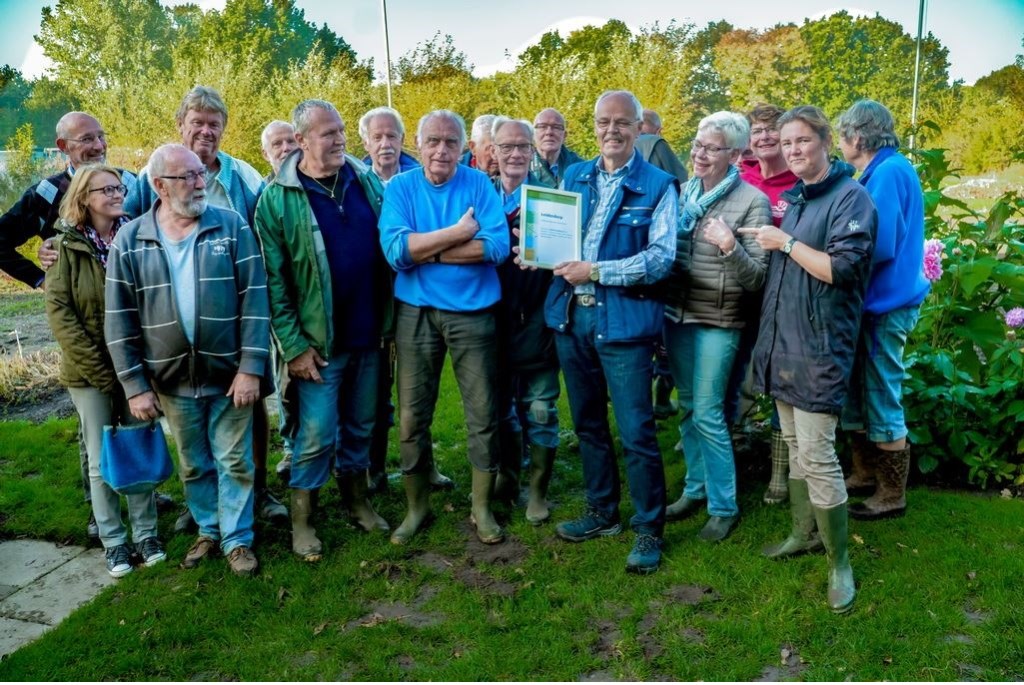 Voorzitter Joop van Huut van de schooltuinen toont de oorkonde, om hem heen staan de onmisbare vrijwilligers van schooltuinencomplex De Sterrekers.