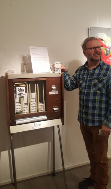 Ro-Nalt Schrauwen opende de expositie en wijst op de ludieke sigarettenautomaat waar je nu een kunstwerkje (Pakje Kunst) uit kunt trekken.