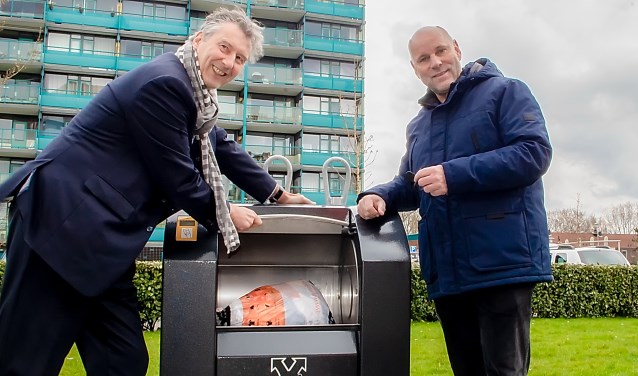 Marc Vooges van Sympany (links) en wethouder Olaf McDaniel hebben de textielcontainer met de elektronische sleutel geopend en doneren een zak textiel.