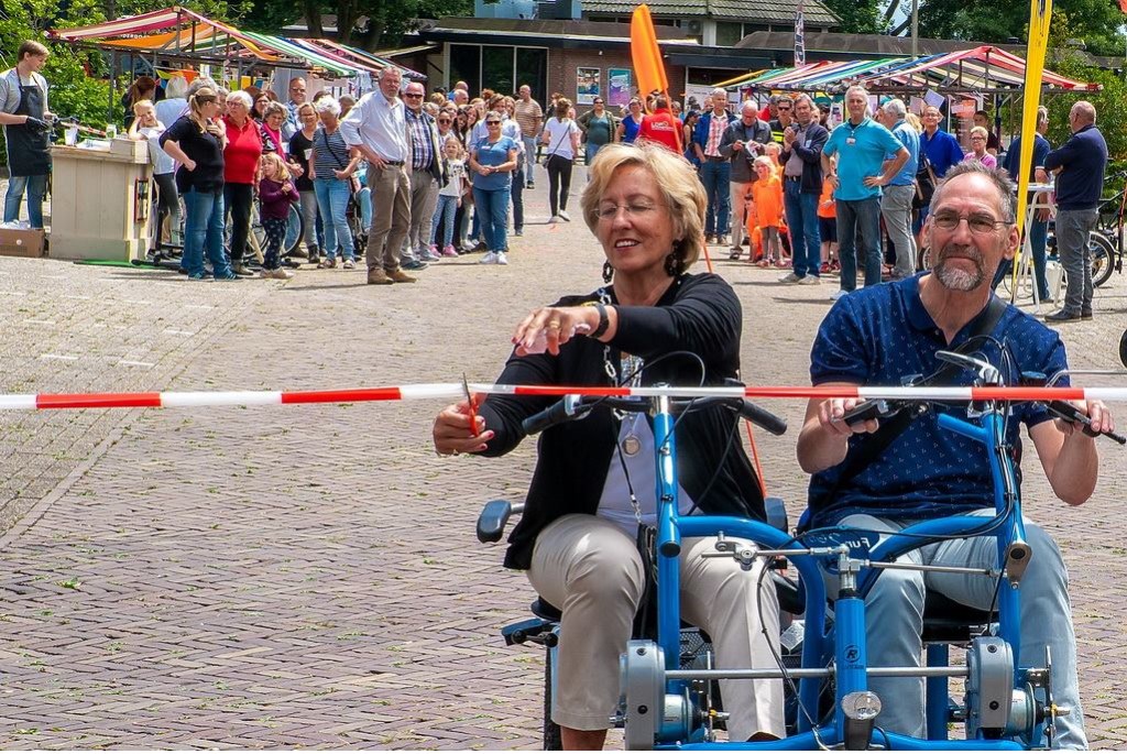 Burgemeester Laila Driessen opent de bewonersmarkt. Naast haar op de duofiets fietsmaatje Jan de Meij.