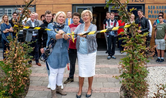 Burgemeester Laila Driessen en lerares Adinda Dernison openen het vergroende plein door een linkt in de beukenboog door te knippen. Net achter hen staan Stefan (links) en Danny, twee van de leerlingen die meegewerkt hebben aan het plan.